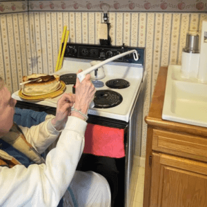 An image of a woman sitting in a wheelchair at the stove using an extended stove knob turner